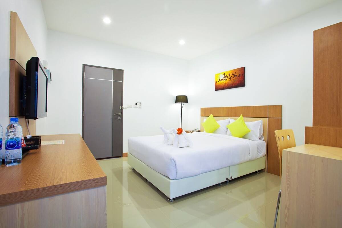 A hotel room with a bed, bedside table, lamp, and a painting on the wall.
