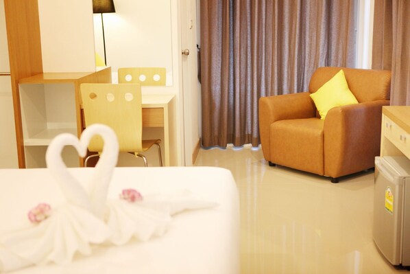 A hotel room with a bed, a desk, a chair, a sofa with a pillow, and a refrigerator.