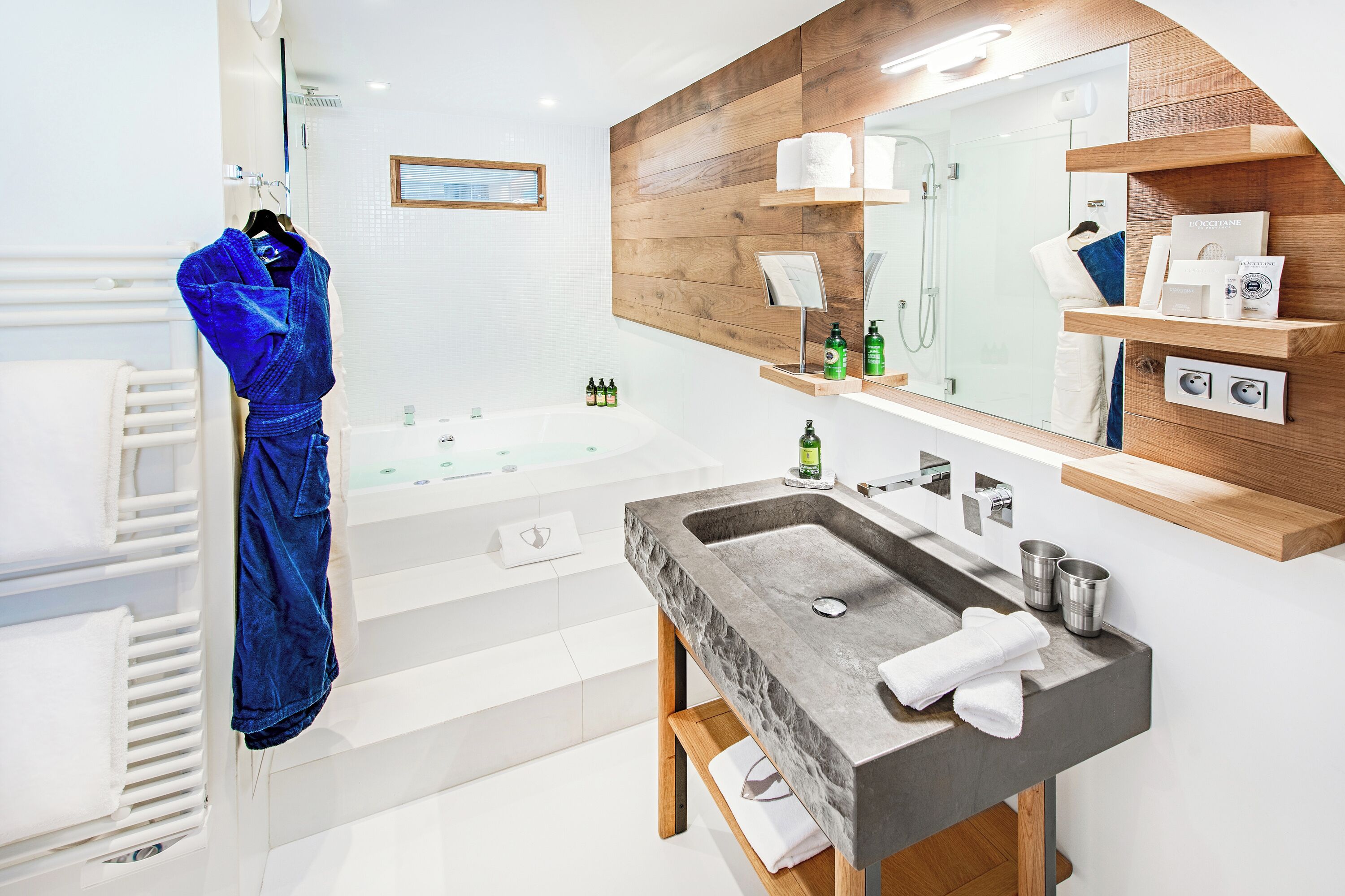 Une salle de bain moderne avec une grande baignoire, un lavabo en granit, des étagères en bois et un peignoir suspendu à un porte-serviettes.