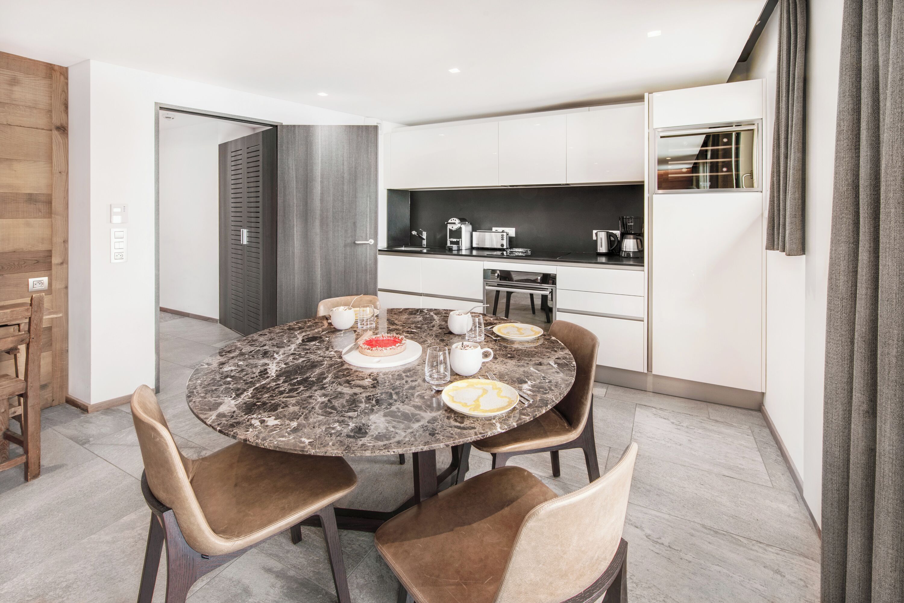 Una cocina moderna con armarios blancos, encimera de mármol y comedor con cuatro sillas y una mesa redonda.