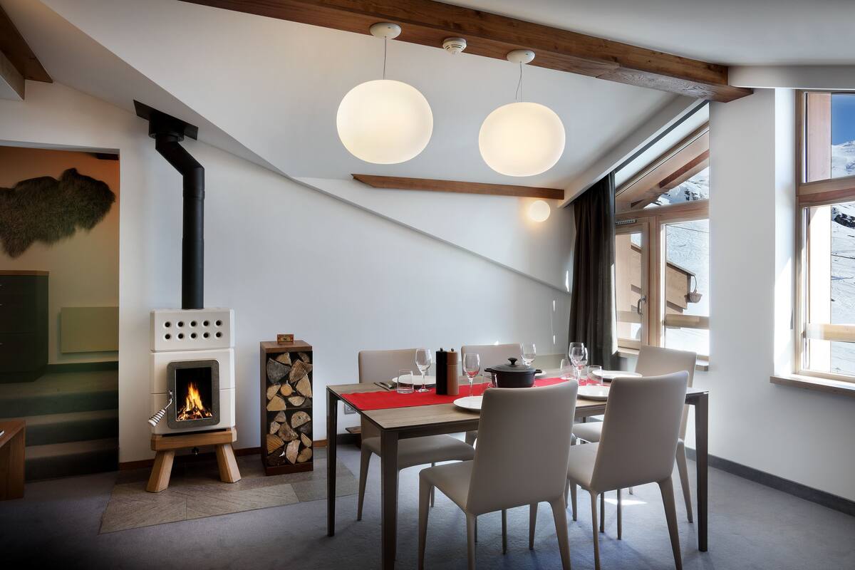 Ein moderner Essbereich mit Kamin, Tisch für vier Personen und großen Fenstern mit Blick ins Freie.