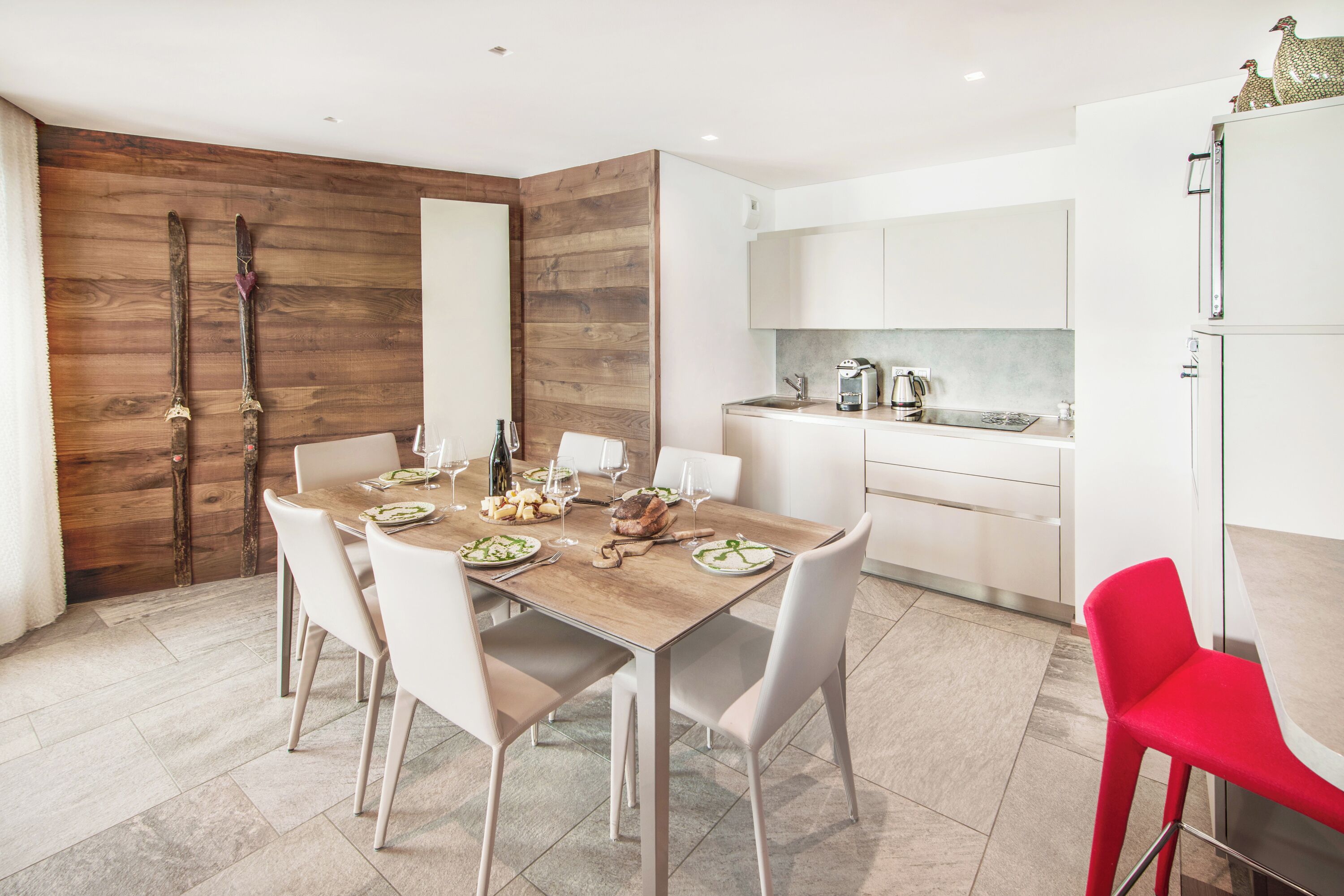 A modern kitchen with white cabinets, a wooden accent wall, and a dining area with a wooden table and white chairs.