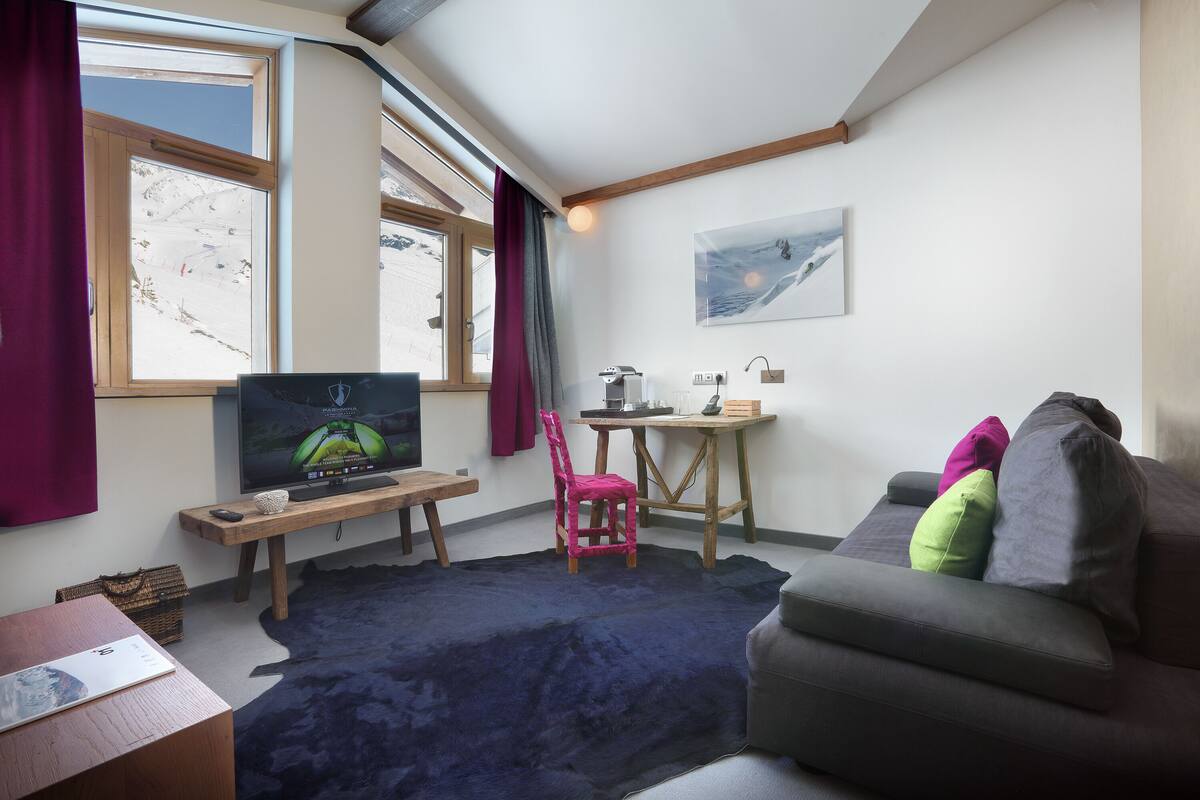 Ein gemütliches Zimmer mit Fernseher, einem Holztisch, einem Stuhl und einem Sofa.