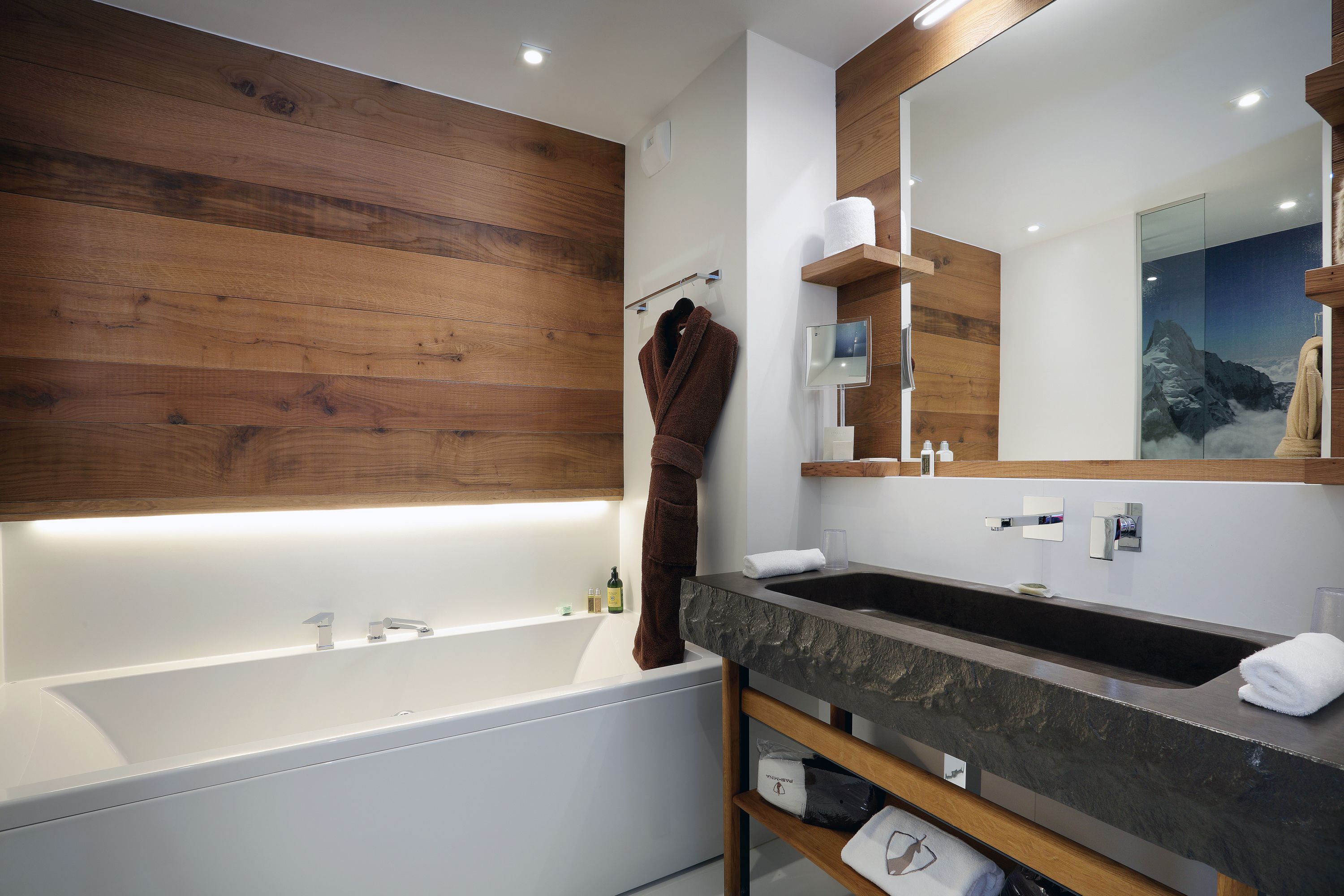 Une salle de bain moderne avec un mur en bois, un grand miroir, une baignoire et un lavabo.