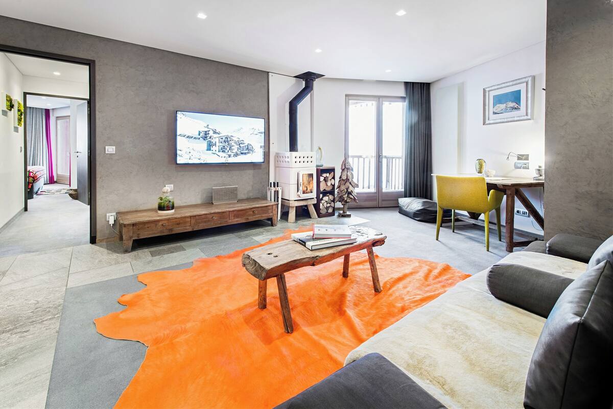 Ein modernes Wohnzimmer mit Kamin, einem an der Wand befestigten Fernseher und einer gemütlichen Sitzecke mit Sofa und Couchtisch.