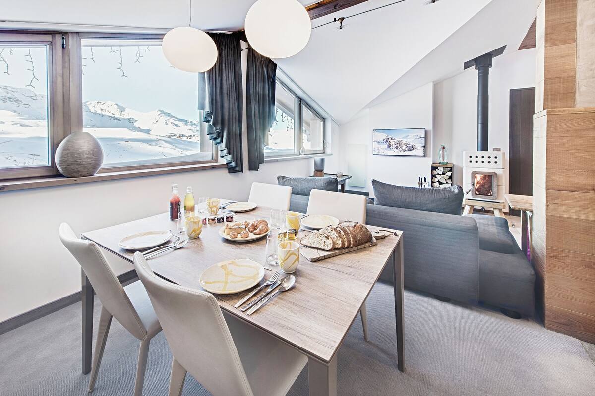 Ein stilvoller Essbereich mit einem Holztisch, gedeckt für das Frühstück, einer Couch und einem Kaminofen.