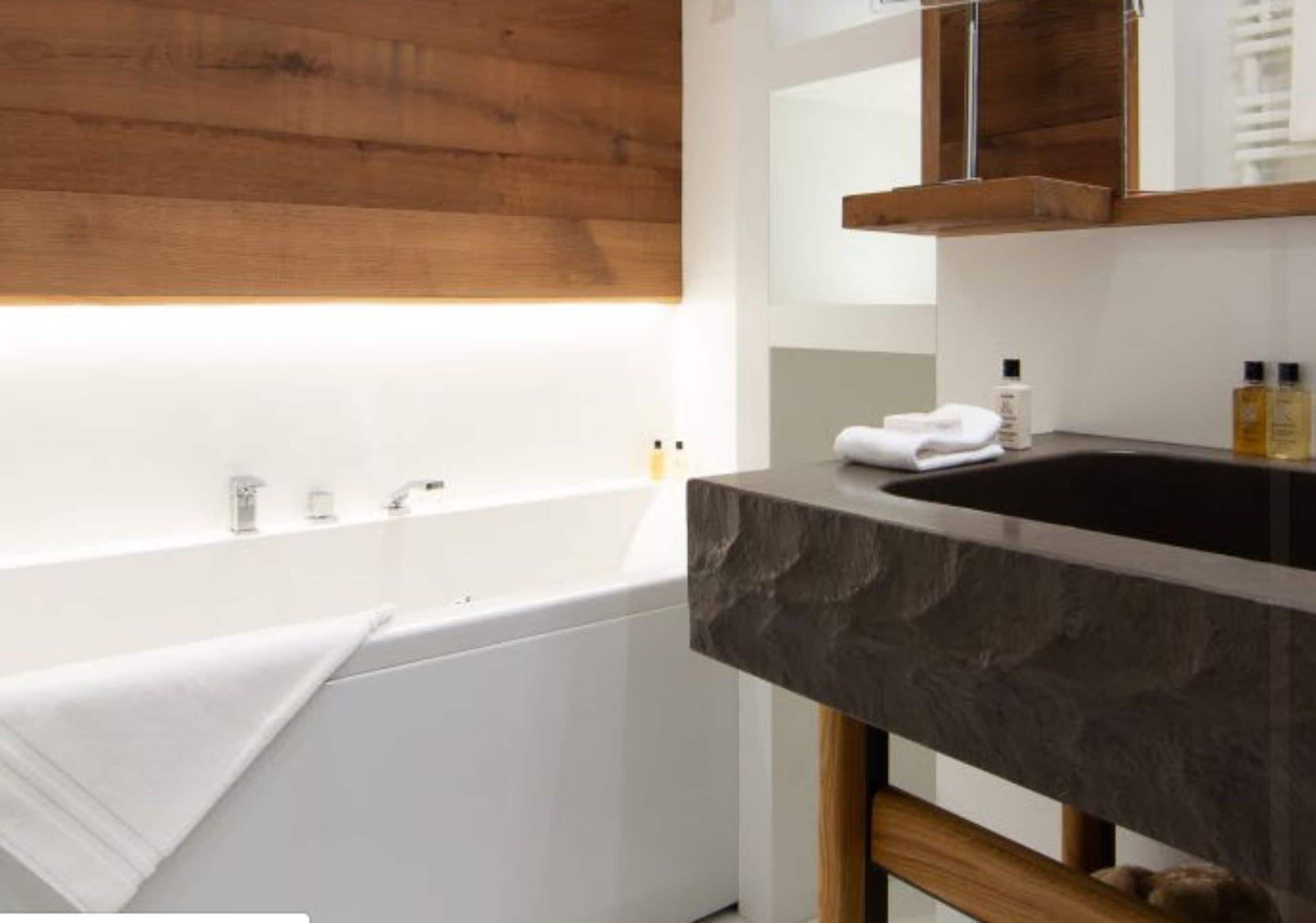 A modern bathroom with a wooden wall, a white bathtub, and a dark marble sink.
