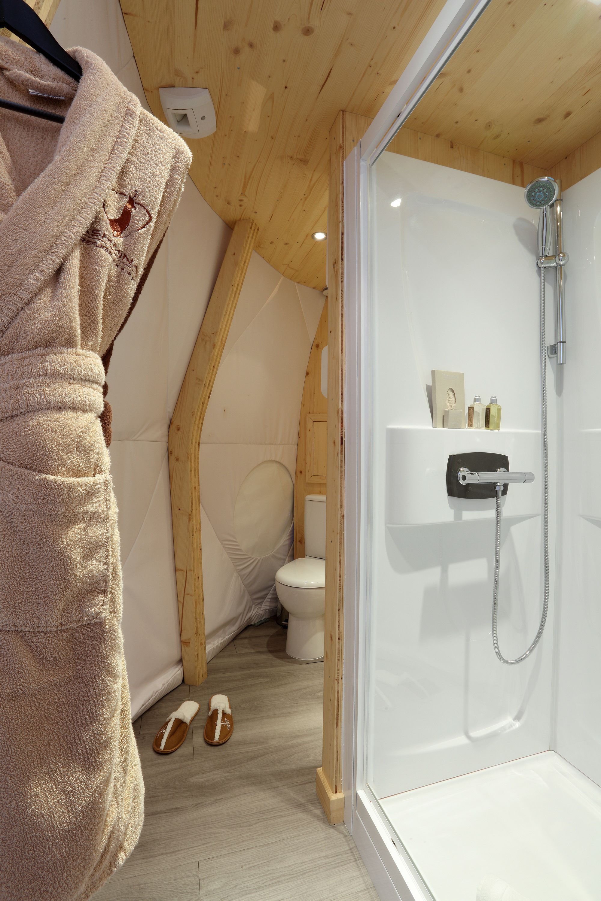 A modern bathroom with a glass-enclosed shower, a wooden ceiling, and a towel hanging on a rack.