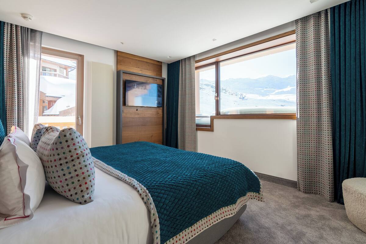 Ein Hotelzimmer mit Bett, Fernseher, Fenster mit Bergblick und Vorhängen.