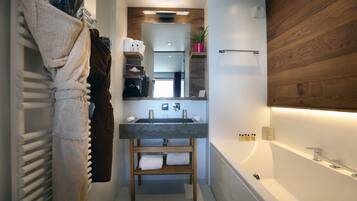 A modern bathroom with a built-in sink, a wooden vanity, a towel rack, and a bathtub.