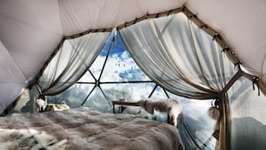 A tented room with a bed, fur rug, and a view of a snowy landscape through the curtains. - Hôtel Pashmina (Les Belleville)