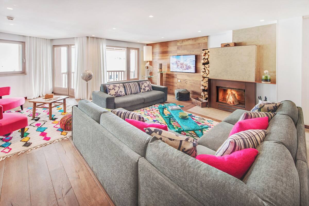 Ein modernes Wohnzimmer mit einem grauen Sofa, einem farbenfrohen Teppich und einem Kamin.