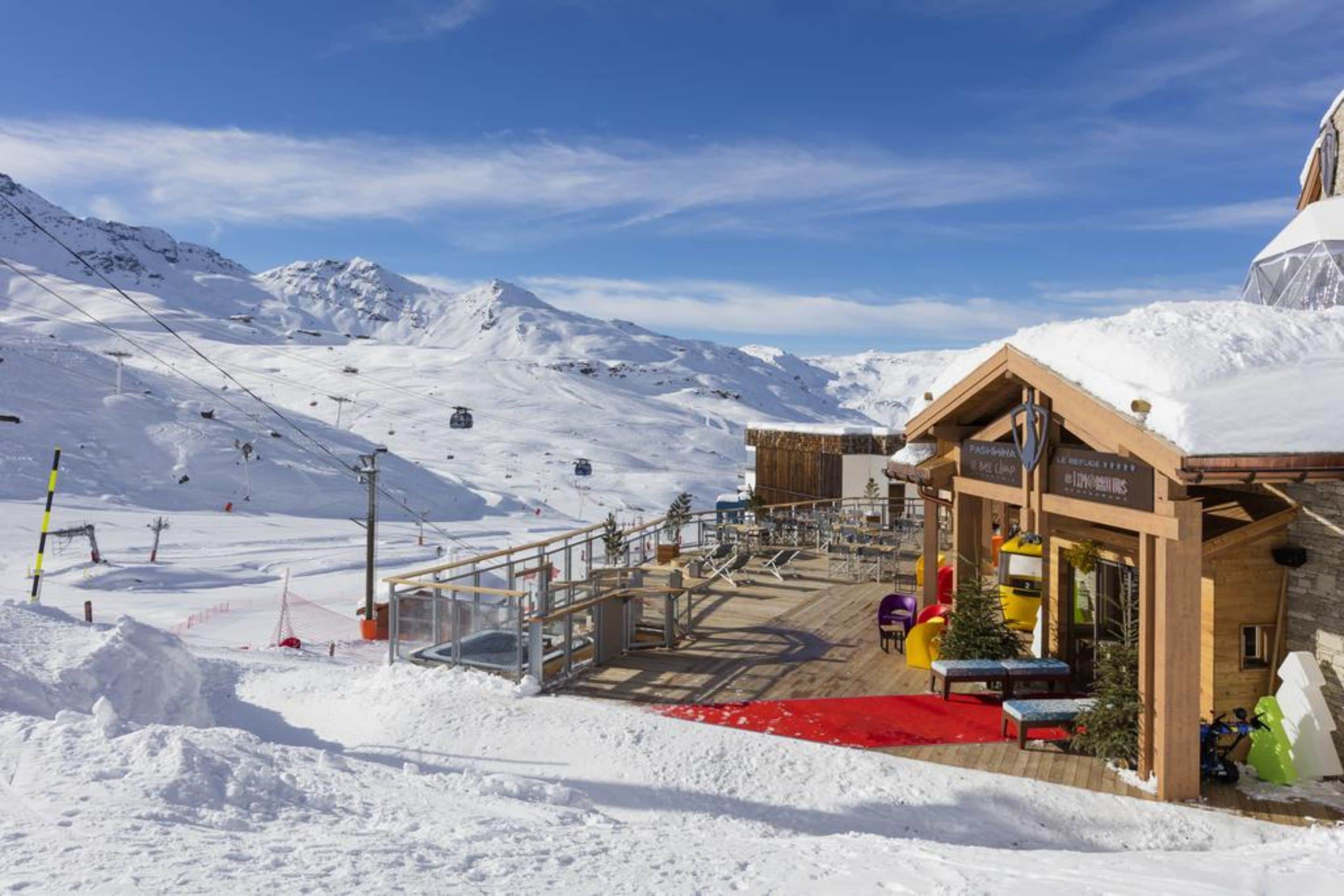 Ein schneebedecktes Bergresort mit einem Holzbauten, einer Seilbahn und einem roten Teppich, der zum Eingang führt.
