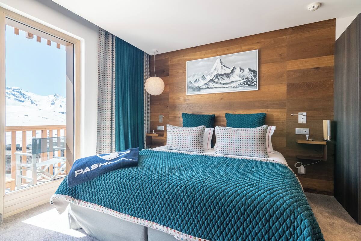 Ein modernes Hotelzimmer mit einem großen Bett, Blick auf einen verschneiten Berg und einem Balkon.