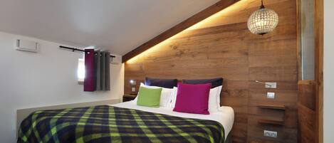 A bedroom with a wooden headboard, a large bed with a plaid bedspread, and a hanging crystal light fixture.