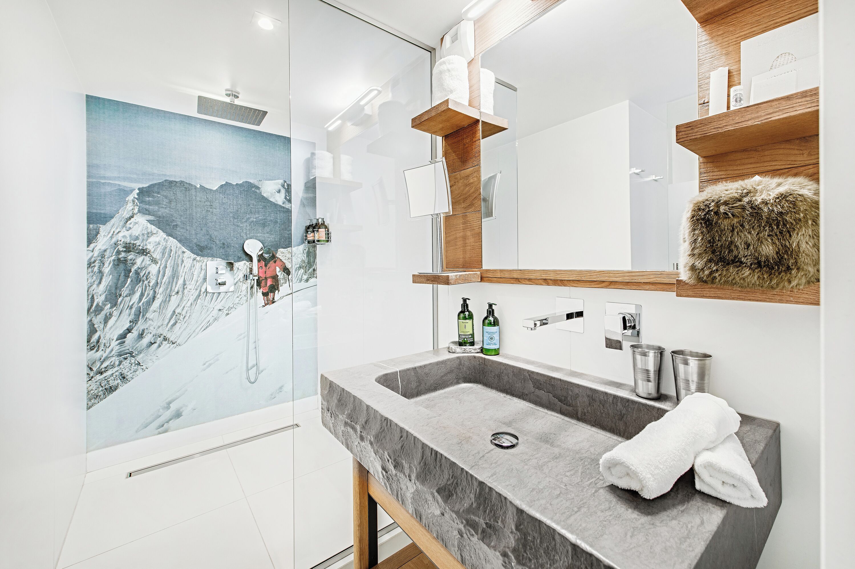 A modern bathroom with a large mirror, marble sink, and a scenic mountain painting on the wall.