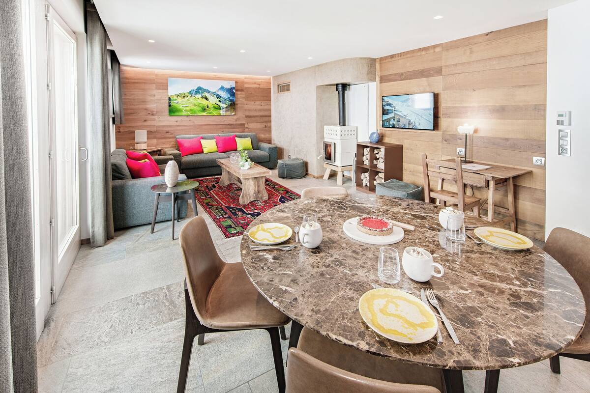 Ein modernes Wohnzimmer mit Kamin, einem Essbereich mit einem Marmortisch und einer Couch mit bunten Kissen.