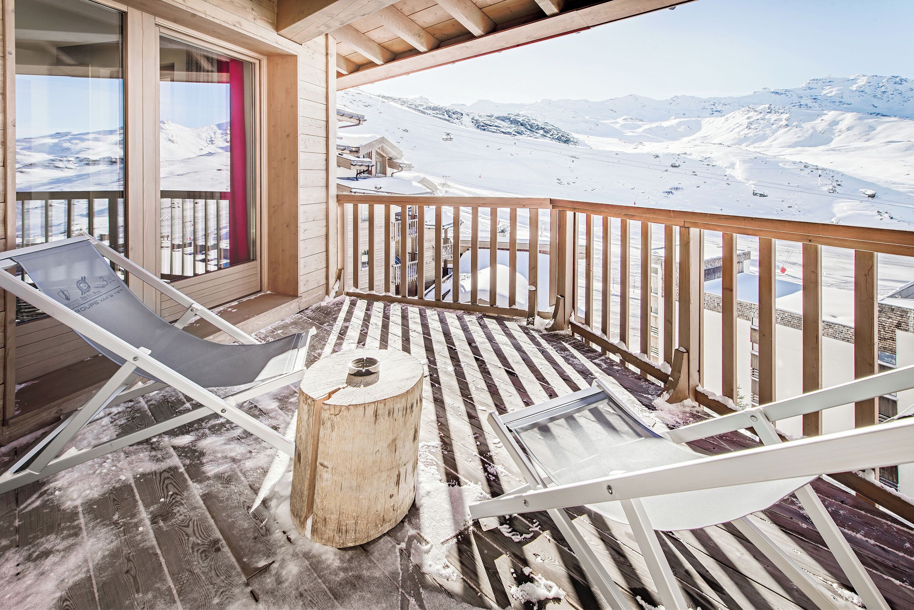 A wooden deck with a glass balustrade, a lounge chair, and a wooden stool.