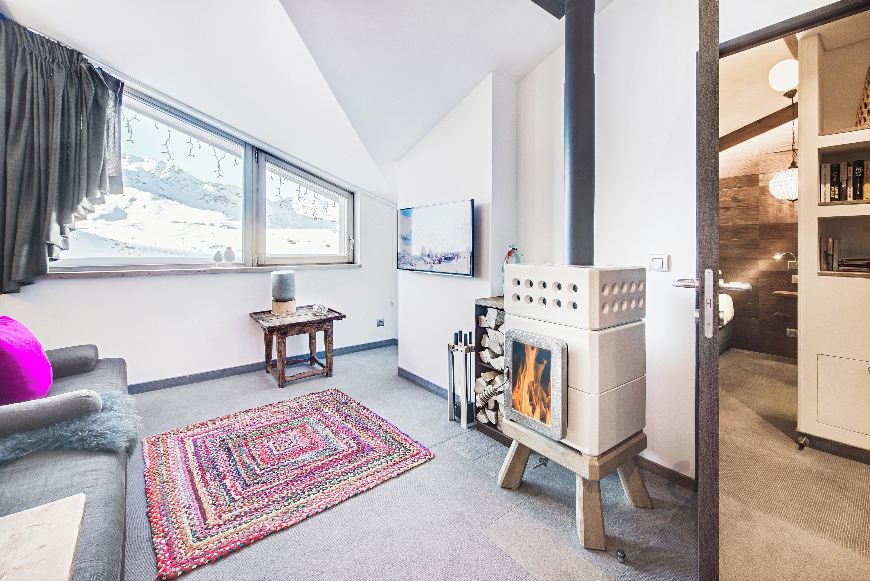 A cozy living room with a fireplace, large windows, and a view of a snowy landscape.
