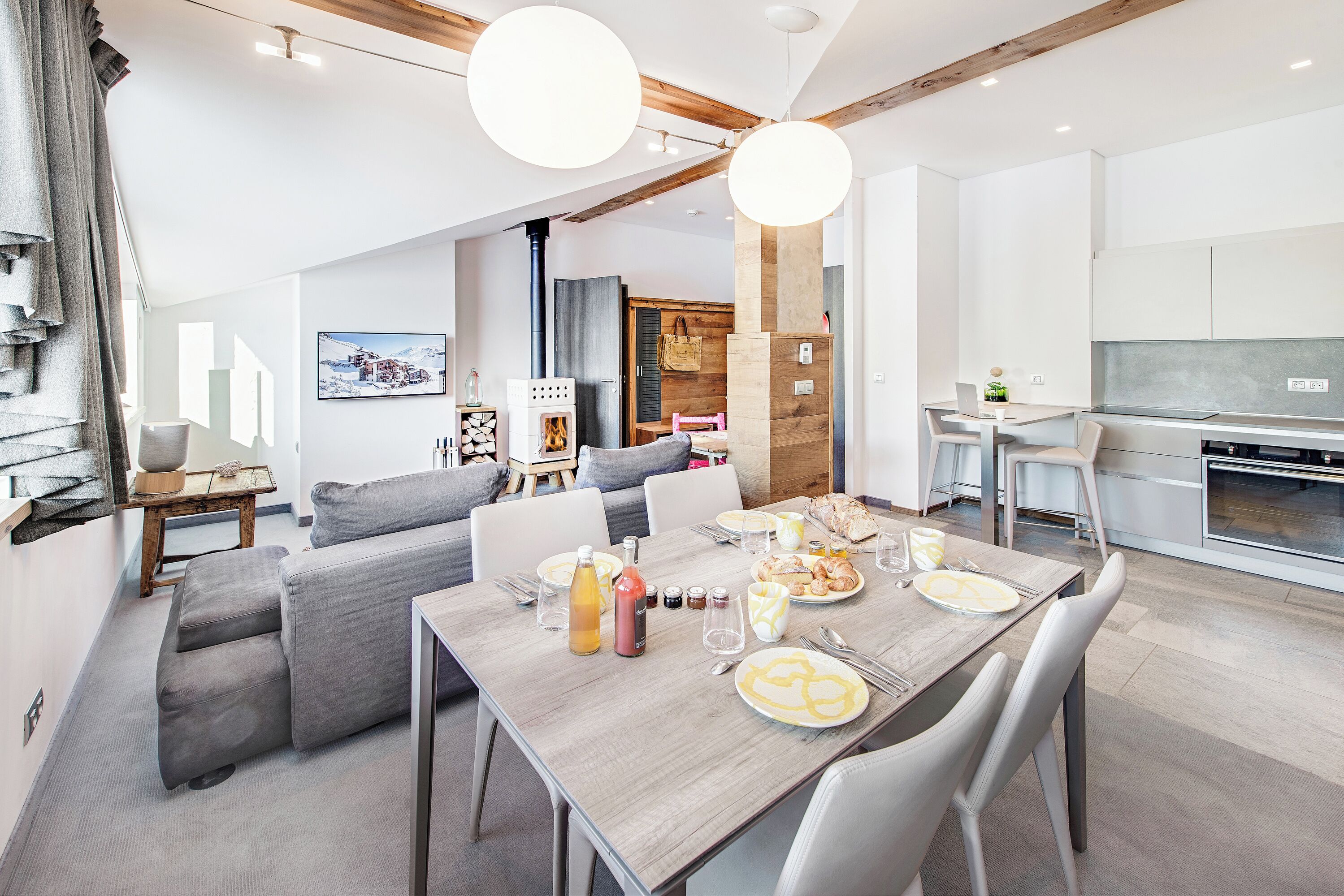 A modern kitchen with a built-in oven and a dining area with a wooden table set for breakfast.