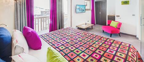 A bedroom with a colorful blanket, a bed, a chair, and a view of the outside.