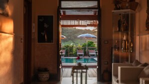 A view through a doorway to a pool area with lounge chairs and umbrellas. - B&B La Mortella (Roccadaspide)