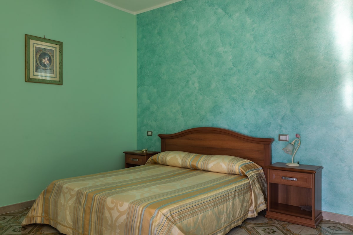 Ein Schlafzimmer mit einem Bett, einem Nachttisch und einem gerahmten Bild an der Wand.