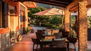 An outdoor patio with wicker furniture and umbrellas, brick pillars, and a stone pathway. - B&B La Mortella (Roccadaspide)