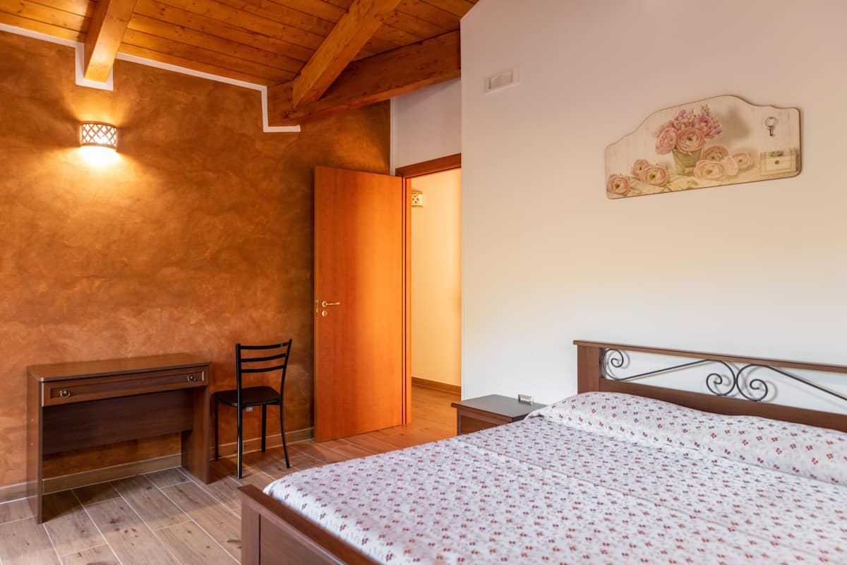 Ein Schlafzimmer mit einem Holztisch, einem Stuhl, einem Bett mit floralem Überwurf und einem an der Wand befestigten Schlüsselhalter.