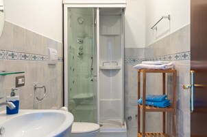 Un baño con cabina de ducha de vidrio, un lavabo blanco y una repisa de madera con toallas.