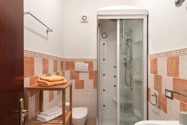 A bathroom with a glass-enclosed shower, a toilet, and a wooden shelf with towels.