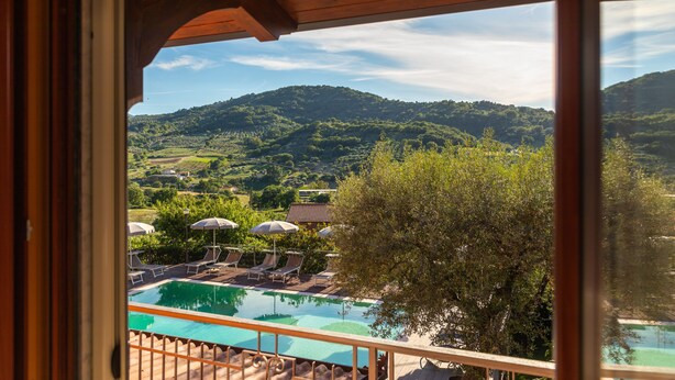 A pool area with lounge chairs and umbrellas, surrounded by lush greenery and hills. - B&B La Mortella (Roccadaspide)