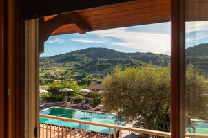 Un área de piscina con sillones de descanso y sombrillas, rodeada de exuberante vegetación y colinas.