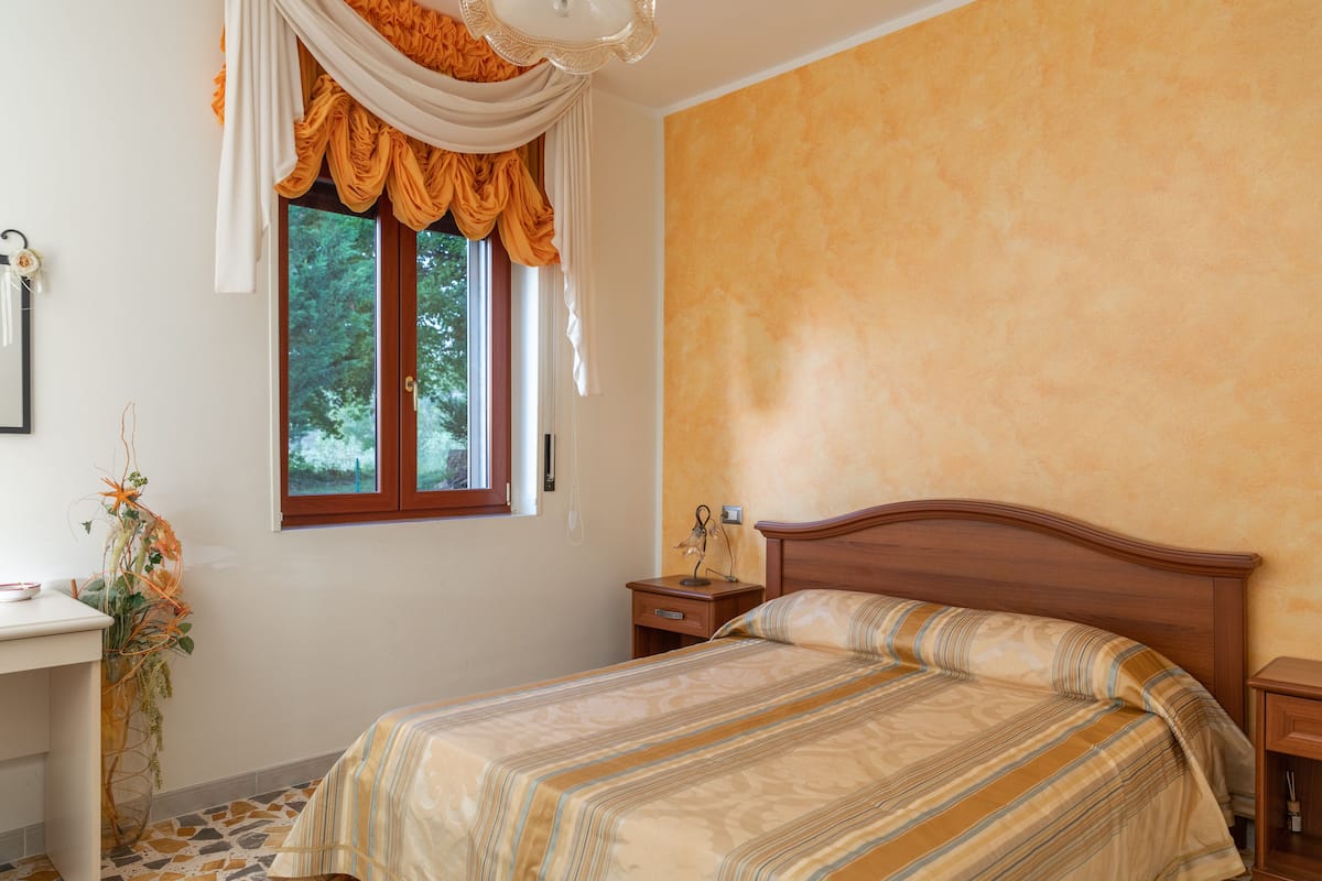 Ein Schlafzimmer mit Bett, Nachttisch, Schreibtisch und einem Fenster mit Vorhängen.