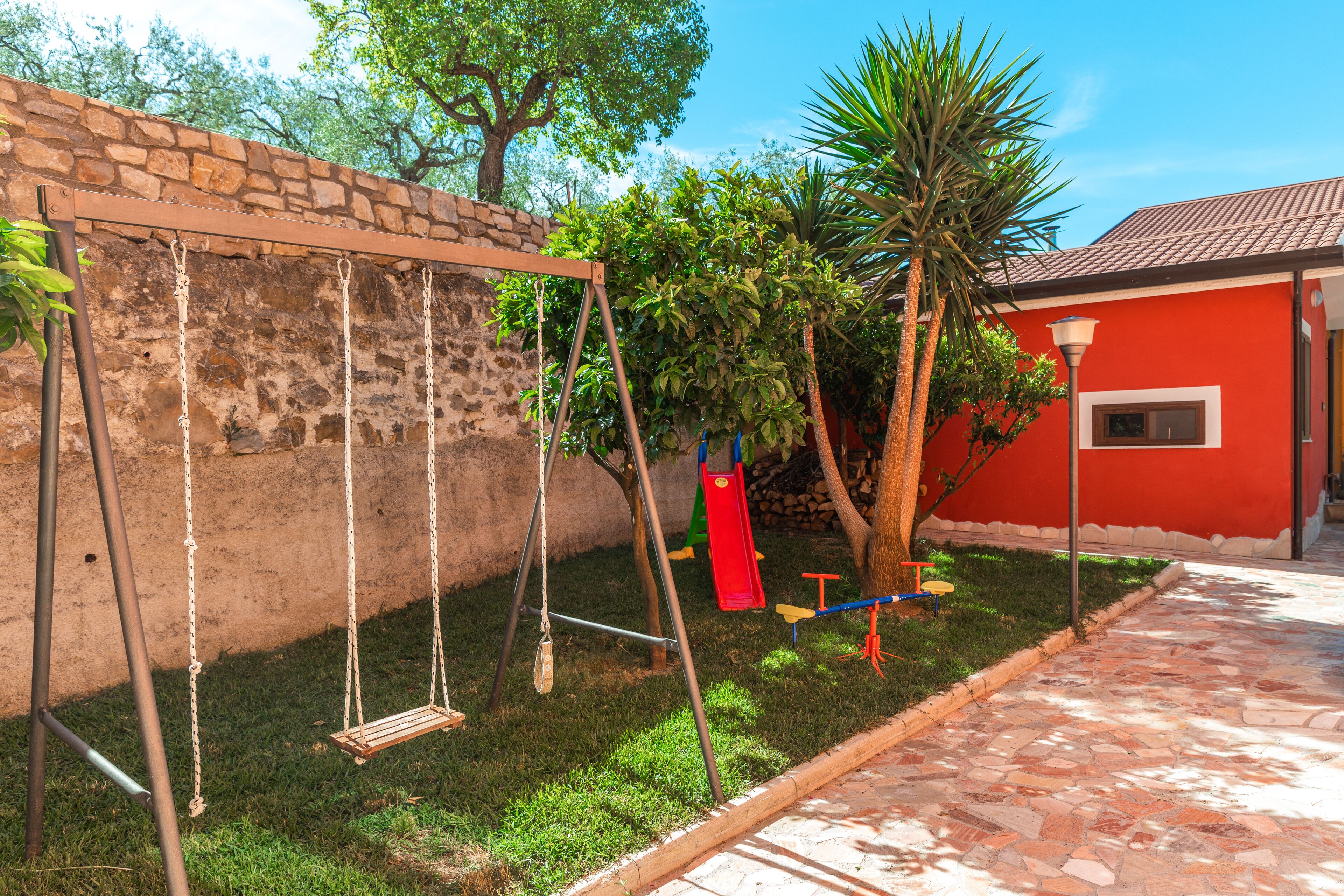 Un jardín con un columpio, un edificio rojo y un muro de piedra.