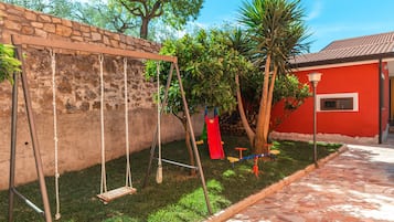 Un jardín con un columpio, un edificio rojo y un muro de piedra.