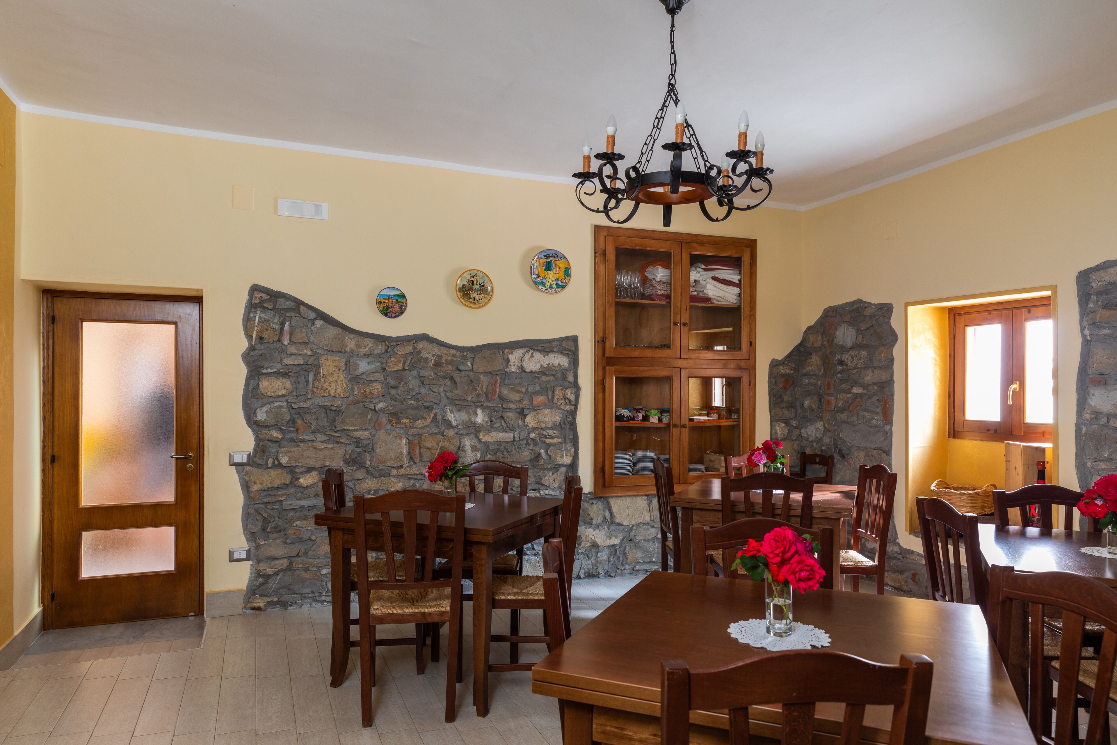 A dining area with wooden tables and chairs, a stone wall, and a chandelier.