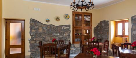 A dining area with wooden tables and chairs, a stone wall, and a chandelier.