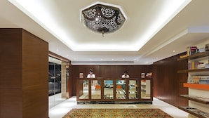 A reception area with a wooden reception desk, a patterned rug, and a ceiling light fixture. - Zone by The Park Bani Park Jaipur (Jaipur)