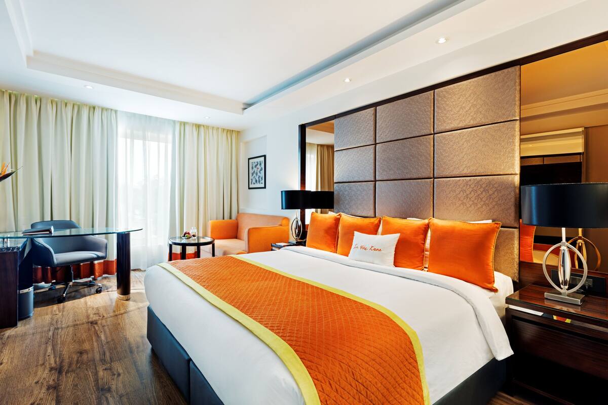 A hotel room with a large bed, a desk, a chair, and a view of the city.