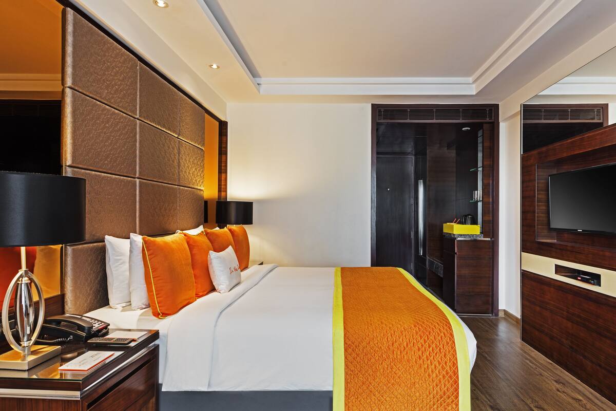 A modern hotel room with a large bed, a TV, and a desk with a telephone and papers.