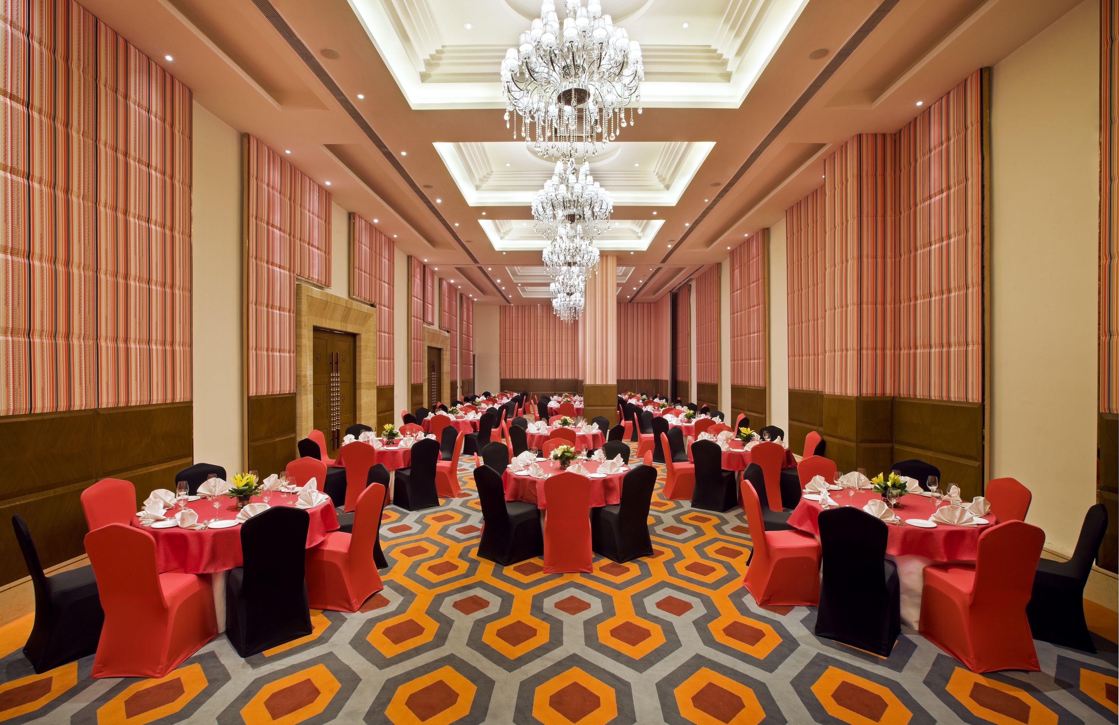 A banquet hall with tables set for a formal event, featuring a geometric patterned carpet and a large chandelier.