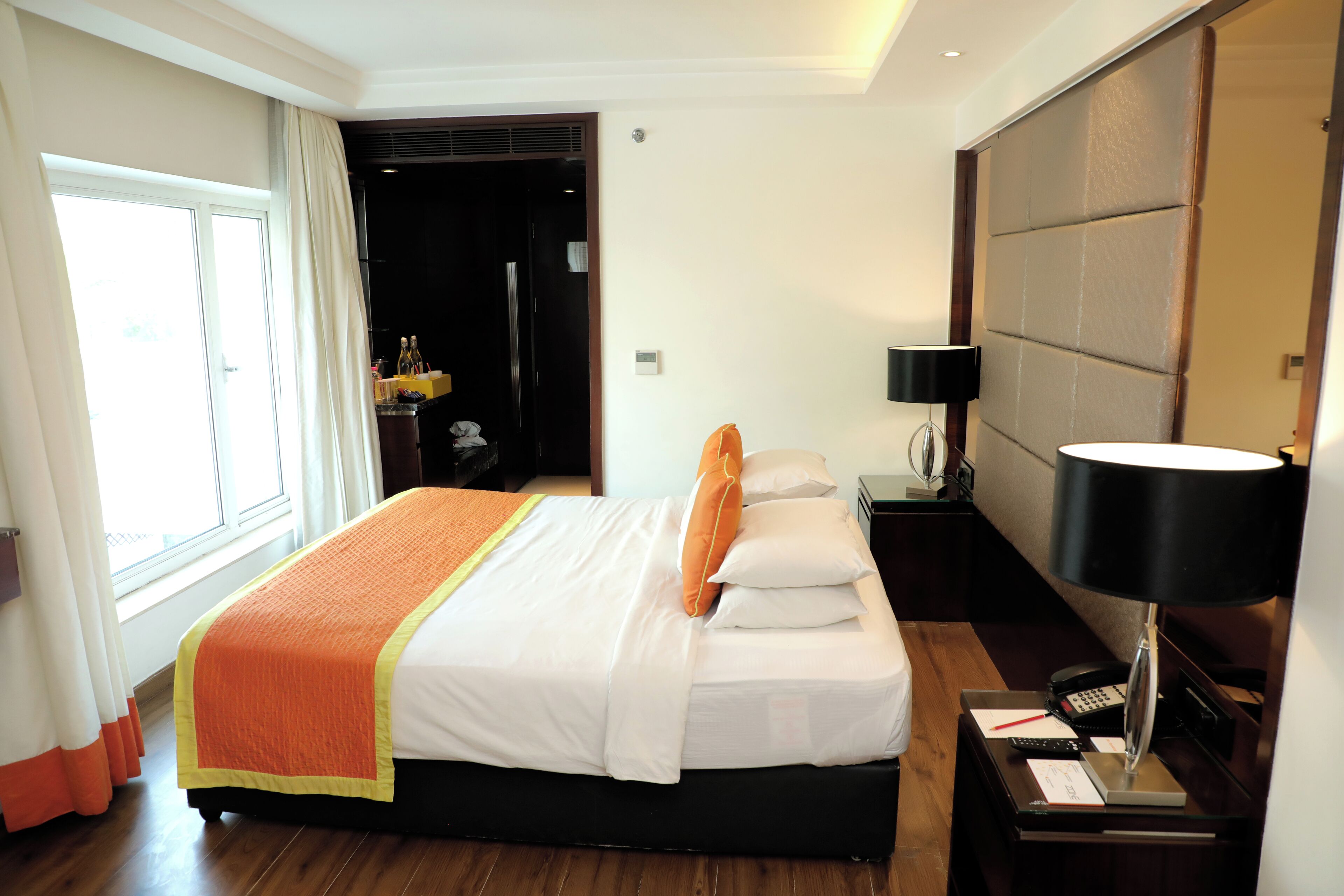 Une chambre d’hôtel avec un grand lit, une table de chevet avec une lampe, une commode et une vue sur un couloir.