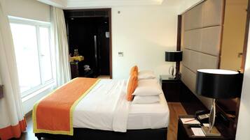 Une chambre d’hôtel avec un grand lit, une table de chevet avec une lampe, une commode et une vue sur un couloir.