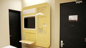Habitació d'hotel amb un llit, una petita taula de nit, un televisor fixat a la paret i una porta amb un senyal.