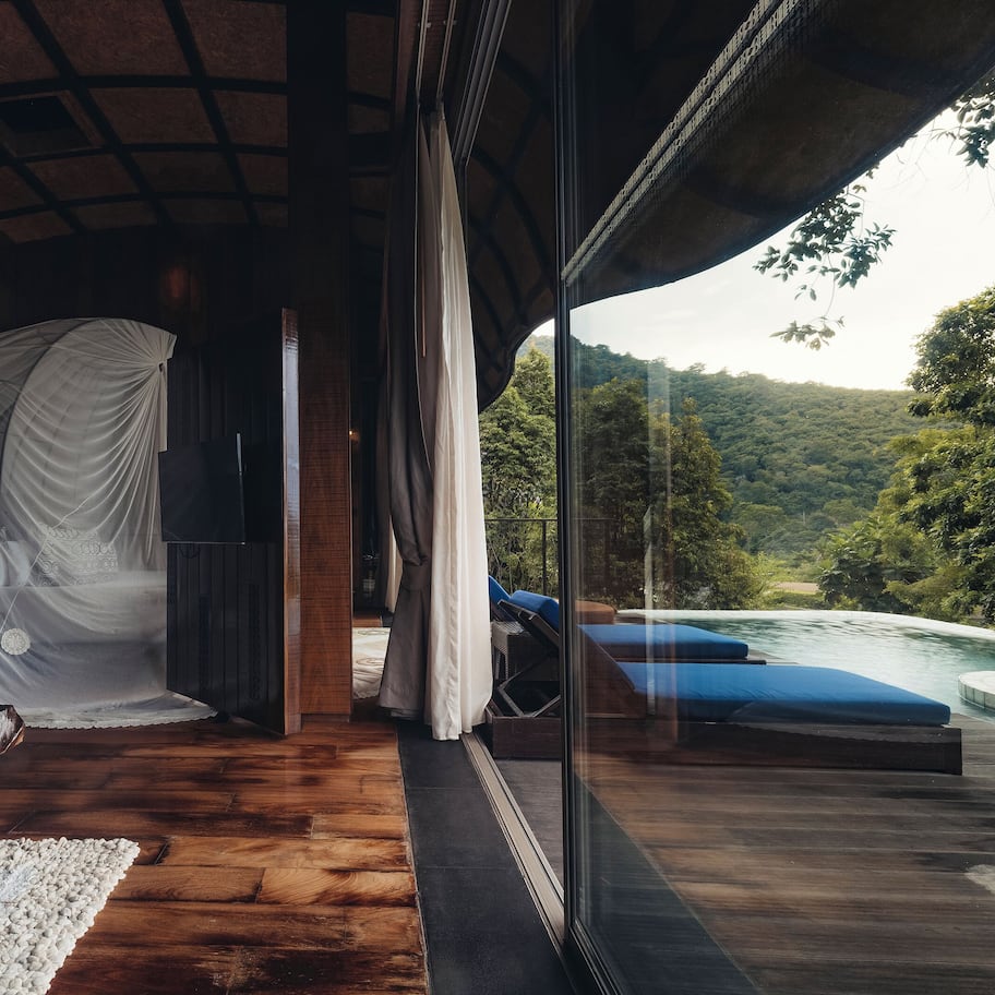 A room with a wooden floor, a glass wall, and a view of a river and forest.