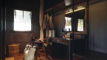 A compact, well-lit room with a wooden desk, a chair, a large mirror, and a window with curtains.
