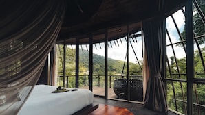 A bedroom with a large bed, a view of lush greenery, and a balcony with a hanging chair. - Keemala (Kamala)