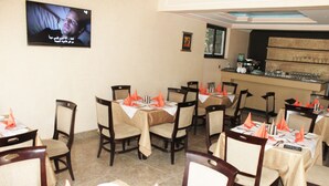 A restaurant with multiple tables set with orange napkins, white tablecloths, and dark wooden chairs. - Southern Addis Hotel (Addis Ababa)
