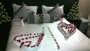 A neatly made bed with white linens, heart-shaped flower arrangements, and decorative pillows. - Southern Addis Hotel (Addis Ababa)